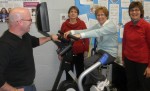 U W 60 minute challenge _Fulton_Y Committee members for the United Way of Greater Oswego County’s 60 Minute Challenge look on as Roberta Dunn practices on a stationary bike. Dunn has partnered with Wendy Tetro to represent Fulton Savings Bank in the event. From left are: Tom Ciappa; Executive Director of the Fulton YMCA, Betty Fadden; Dunn, and Resource Development Director for the United Way of Greater Oswego County, Lois Luber. Absent are committee members; Deana Masuicca, executive director of the Oswego YMCA; John and Tara Fitzgibbons of Fitzgibbons Real Estate; executive director of the United Way, Melanie Trexler; Chrissy Mason of Stability Fitness; and Kim McPherson of the Fulton YMCA.