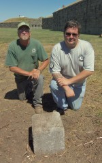 Fort Ontario Maintenance Staff Member Gary Wilson and AmeriCorps Member Matthew Harmer pose beside the rediscovered lighthouse marker.